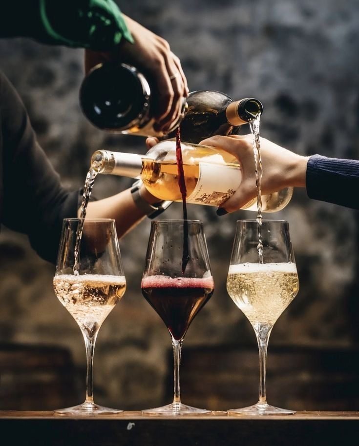 Wine being poured into three raised glasses in golden light