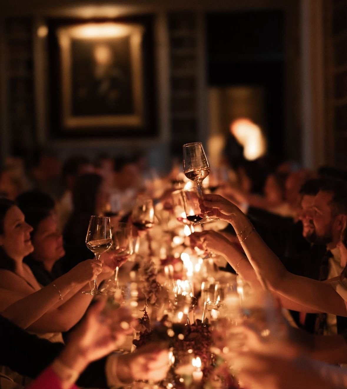 Guests raising glasses in a toast across the candlelit table