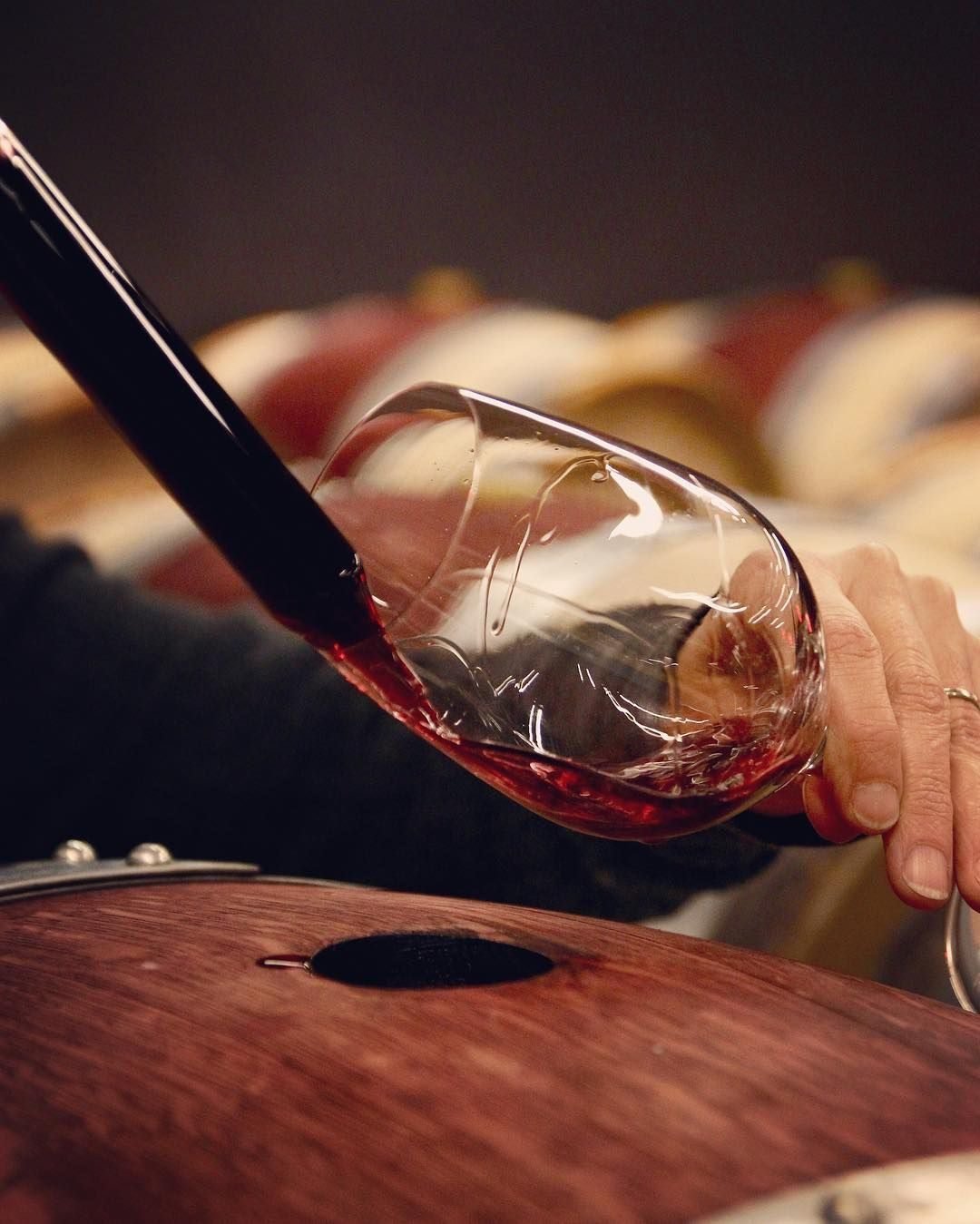 Red wine being poured into a large glass in a dim cellar
